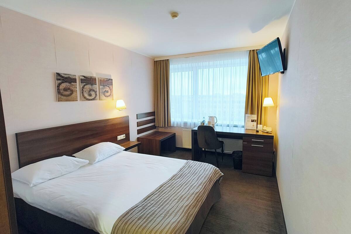 A hotel room with a bed, desk, chair, and a TV mounted on the wall.