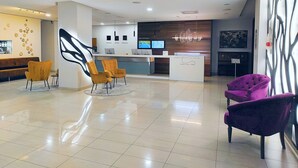 Un área de recepción moderna con mostrador, asientos y una pantalla digital que muestra una lista de destinos.