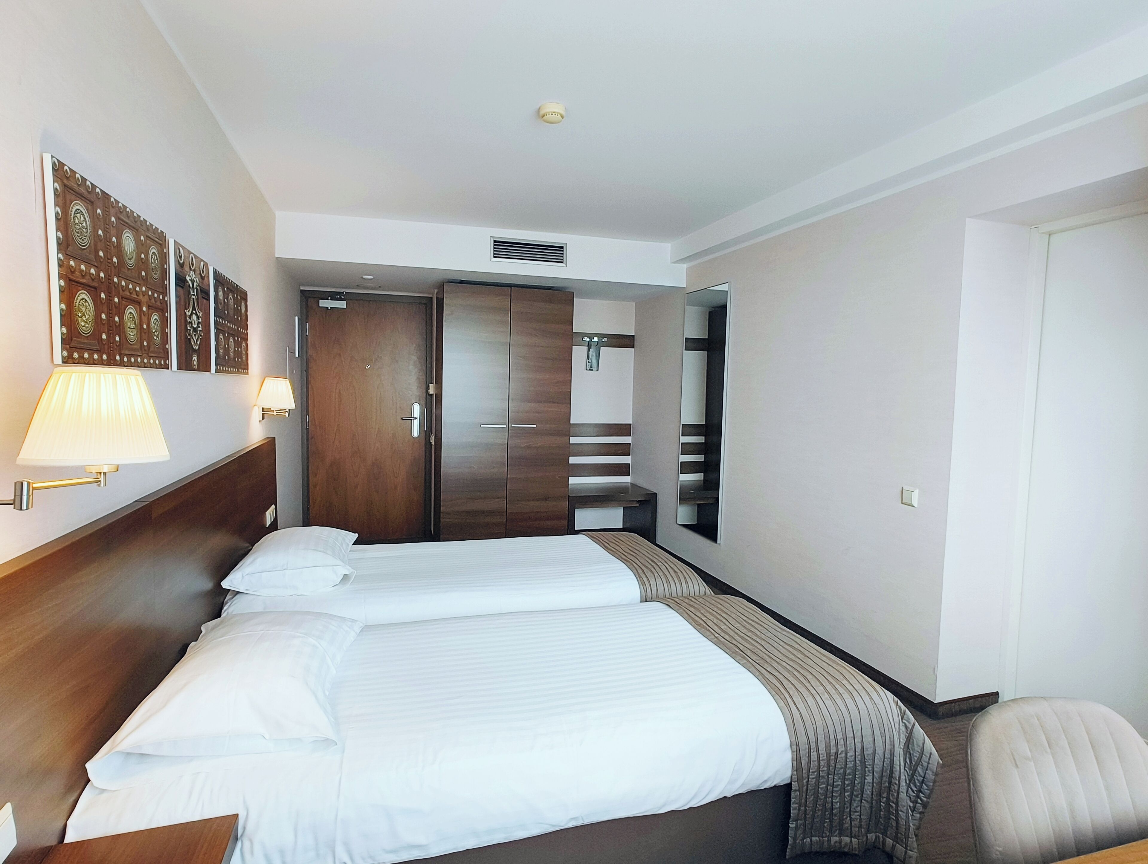 A hotel room with a large bed, a wooden wardrobe, a mirror, and a desk.