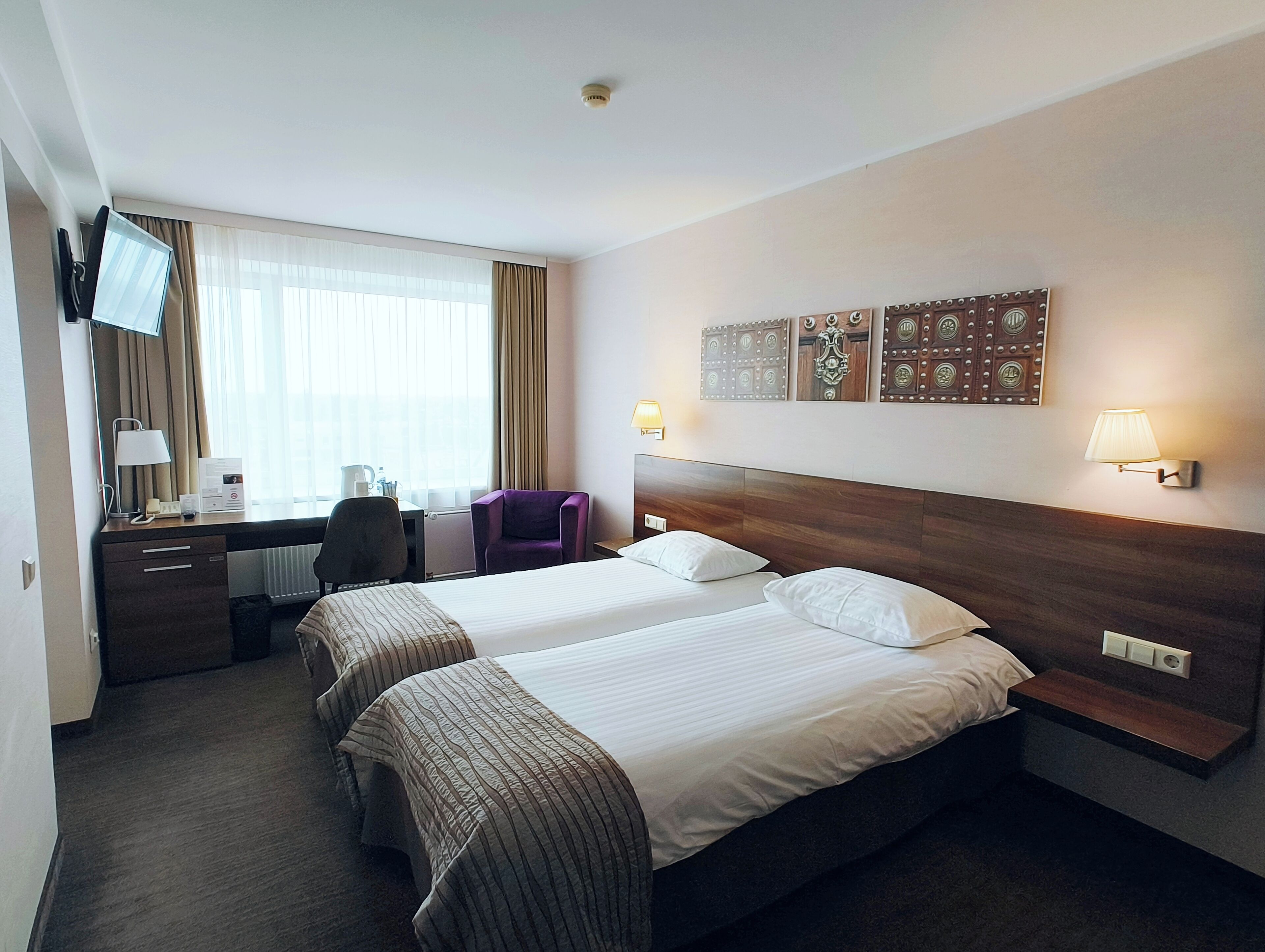 Une chambre d’hôtel avec deux lits, un bureau avec une chaise, une télévision et des œuvres d’art décoratives au mur.