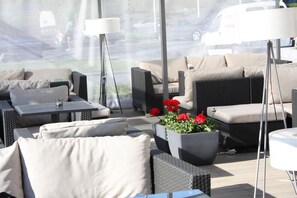 An outdoor seating area with wicker furniture, a table, and a potted plant with red flowers. - Mercure Marijampole (Marijampole)