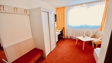A hotel room with a red carpet, a desk with a chair, a small table with a chair, and a bed.