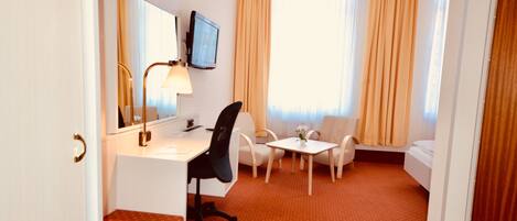 A hotel room with a desk, chair, small table, and sofa.