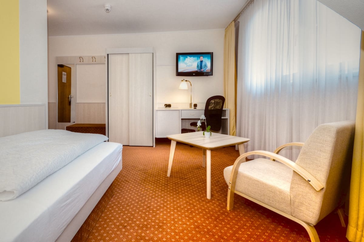 Ein Hotelzimmer mit Bett, Schreibtisch, Stuhl, Fernseher und einem Fenster mit Vorhängen.