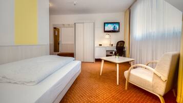 A hotel room with a bed, a desk, a chair, a TV, and a window with curtains.