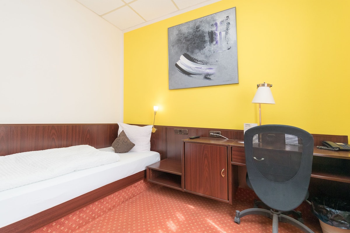Ein Hotelzimmer mit einem Bett, einem Schreibtisch, einem Stuhl, einer Lampe und einem Bild an der Wand.