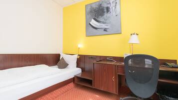 A hotel room with a bed, a desk, a chair, a lamp, and a painting on the wall.
