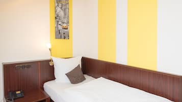 A hotel room with a bed, a bedside table with a phone, and a wall with a yellow and white striped pattern.