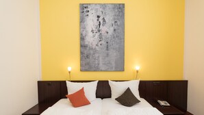 A double bed with white bedding, two bedside tables, a telephone, and a wall-mounted painting.
