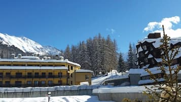 Ein schneebedecktes Gebäude mit mehreren Balkonen, ein Berg im Hintergrund und mit Schnee beladene Bäume.