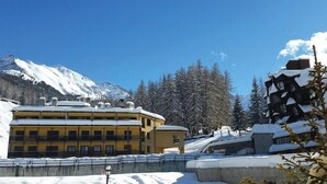 Un edificio cubierto de nieve con múltiples balcones, una montaña al fondo y árboles cargados de nieve.