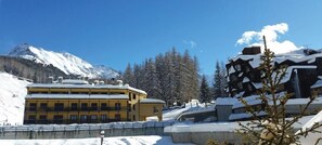 Un edificio cubierto de nieve con múltiples balcones, una montaña al fondo y árboles cargados de nieve.