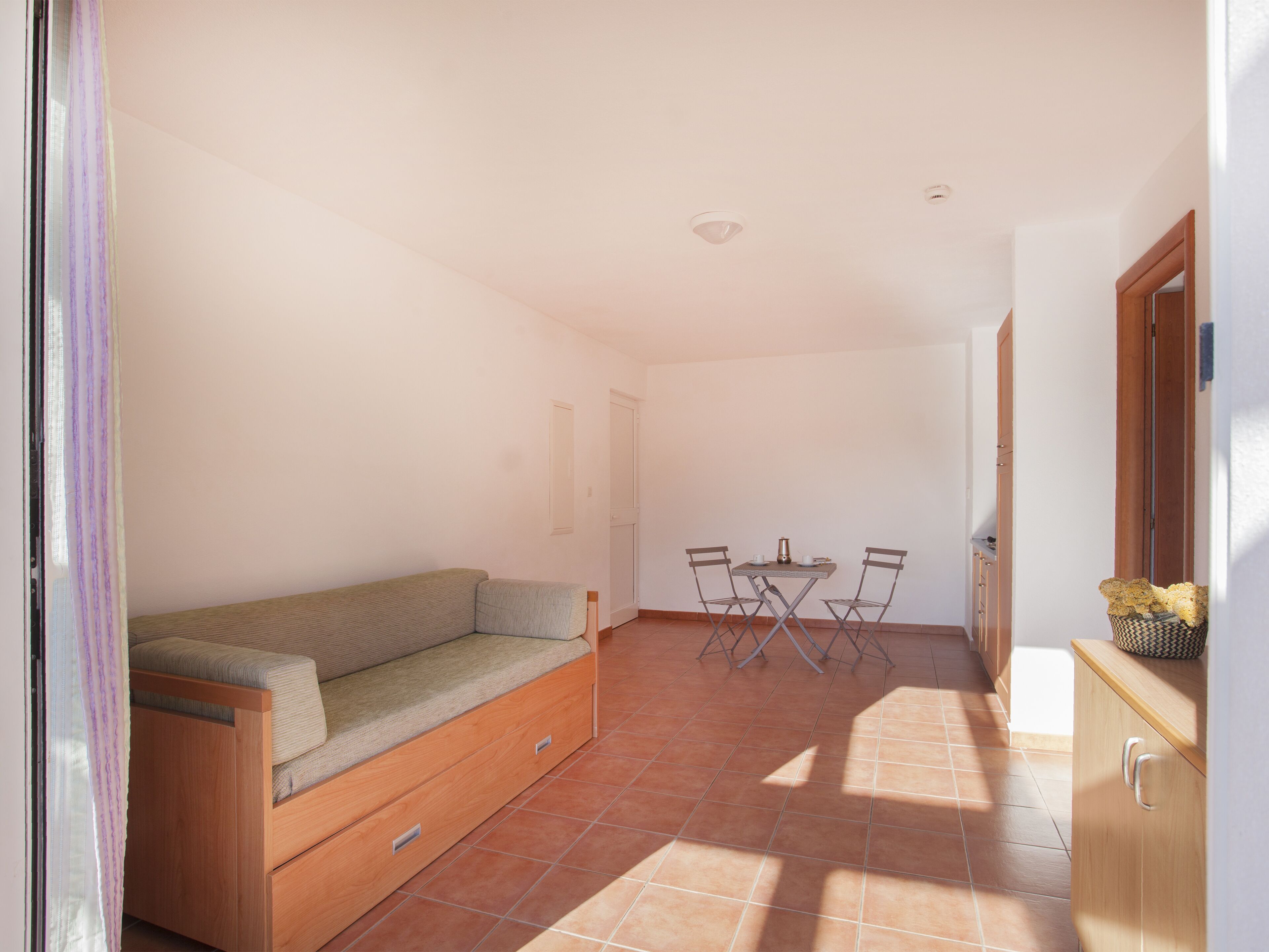 Una habitación con un sofá, una pequeña mesa con sillas y un armario.