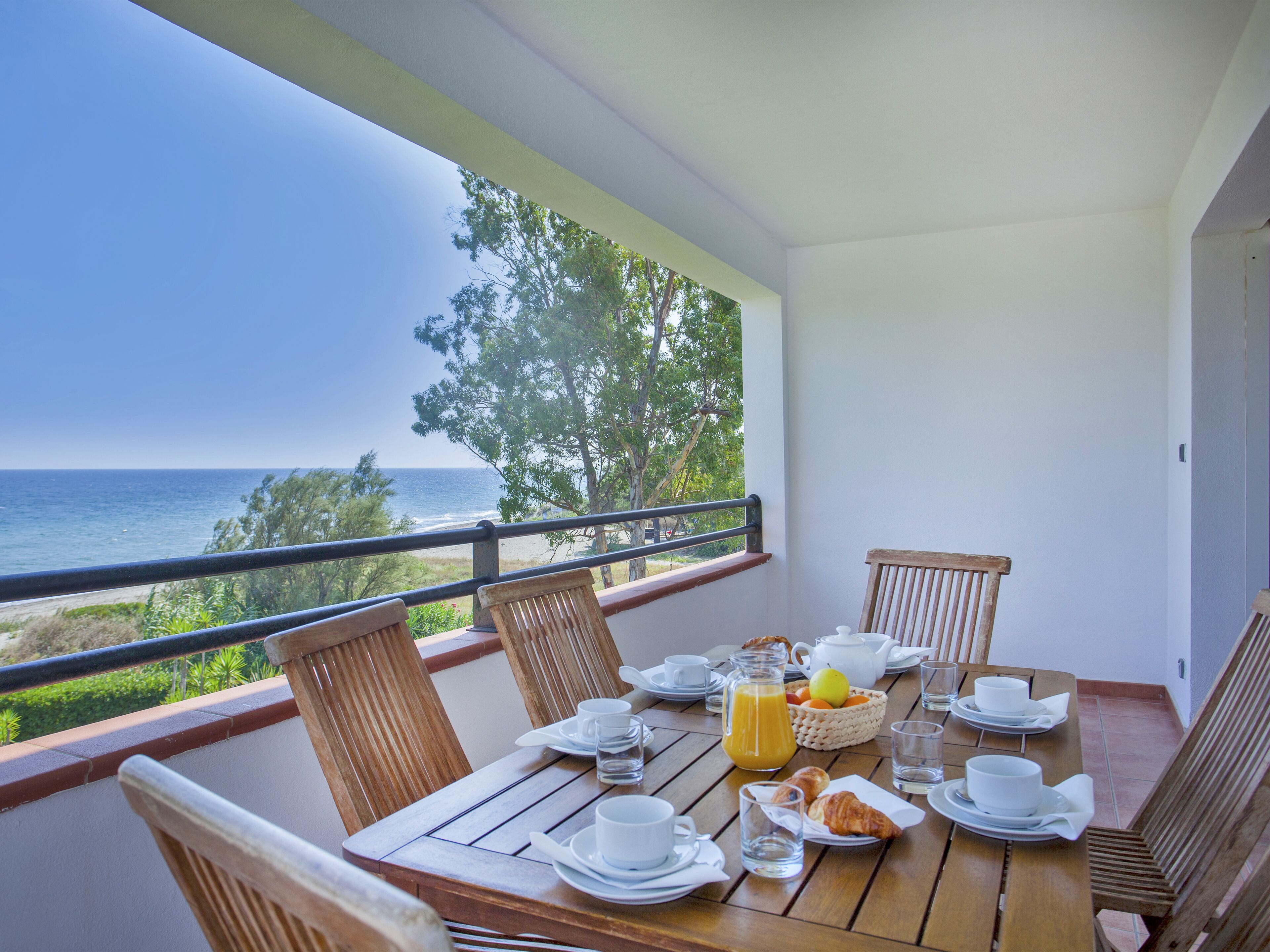 Una mesa de madera preparada para el desayuno con vistas al océano.