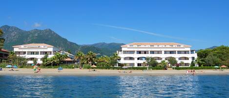 A beachfront hotel with multiple balconies, a sandy beach, and palm trees.