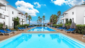 A swimming pool with blue water, surrounded by white buildings and palm trees. - Vacanceole Sognu Di Rena (San-Nicolao)