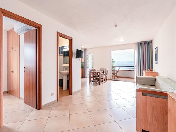 A spacious living area with a dining table, a sofa, and a view of the sea.