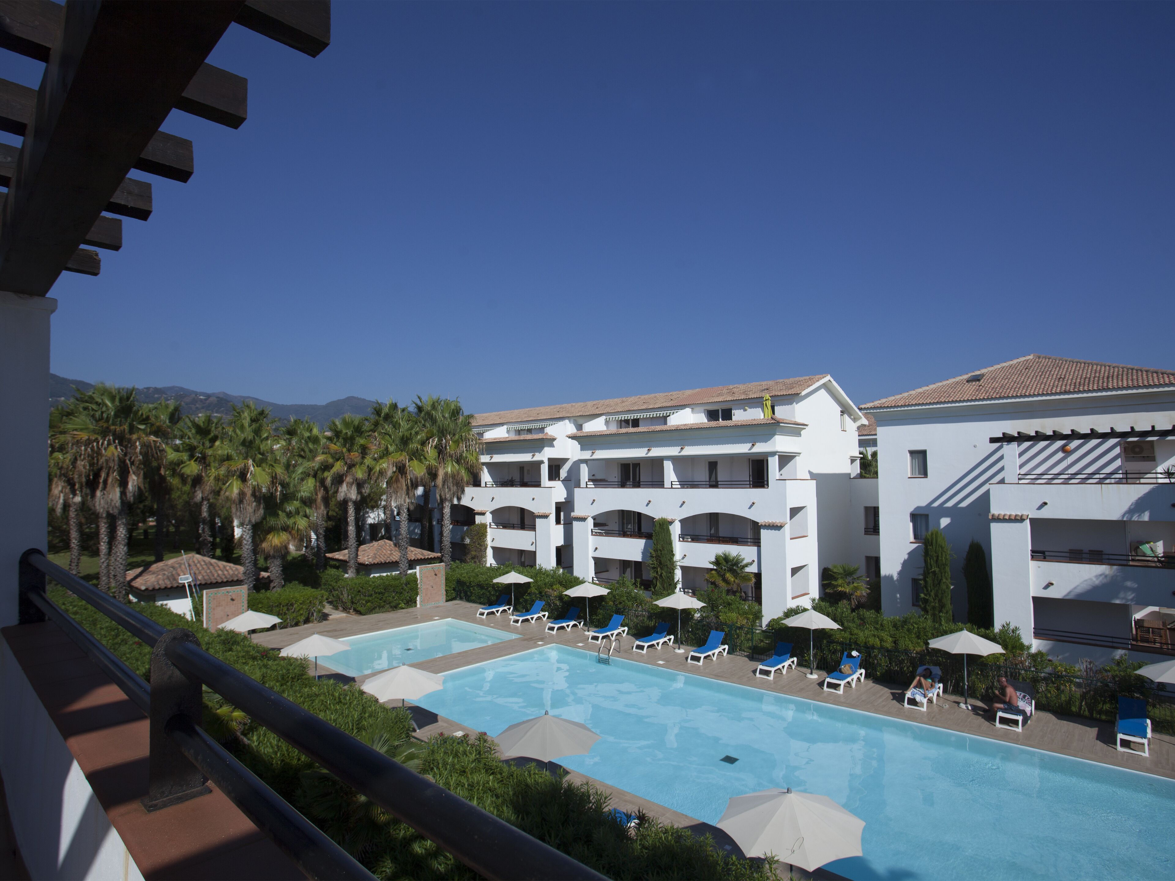 A hotel with a pool area, multiple balconies, and palm trees.