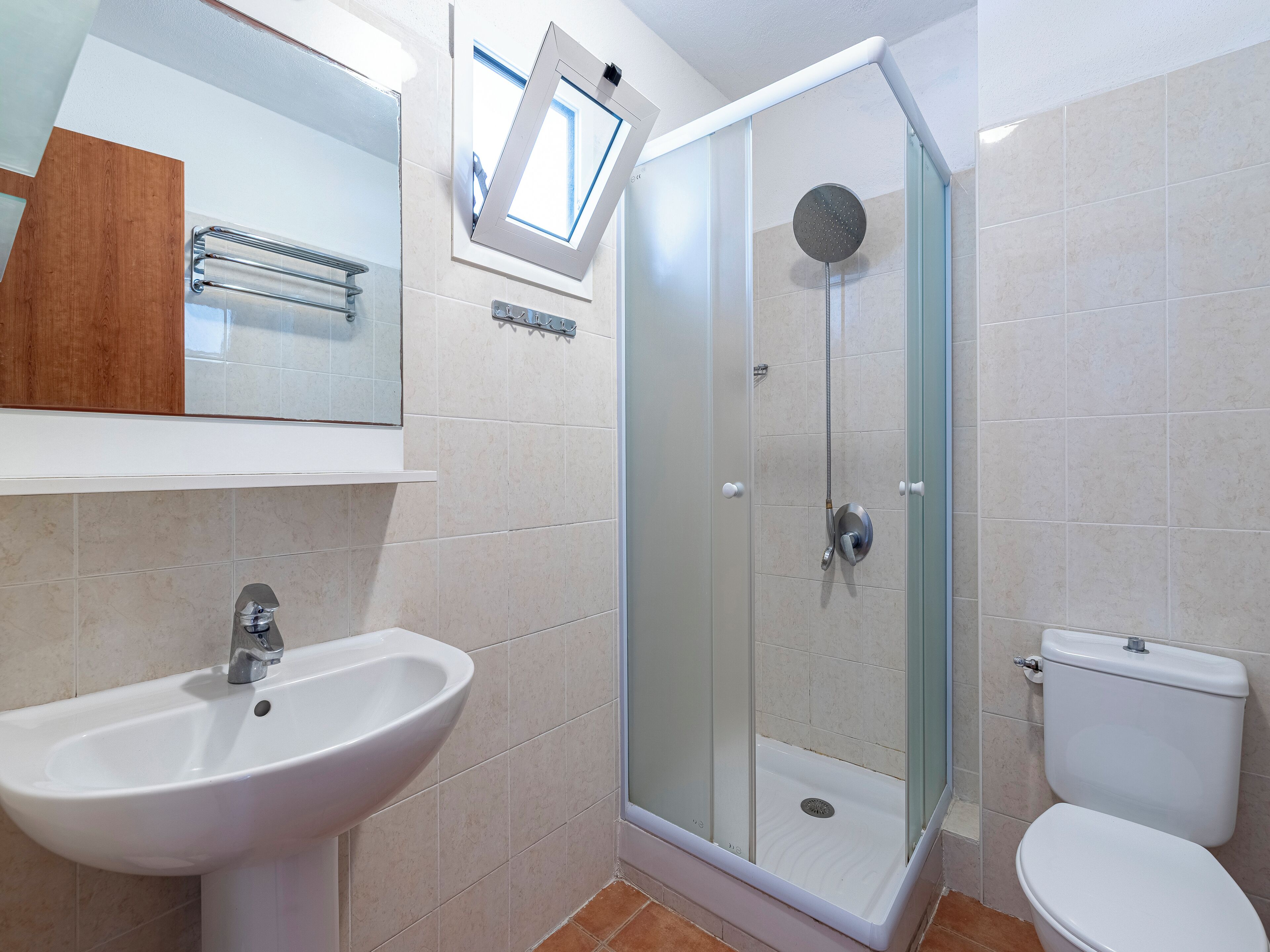 Un baño moderno con ducha envuelta en vidrio, lavamanos blanco y un inodoro.