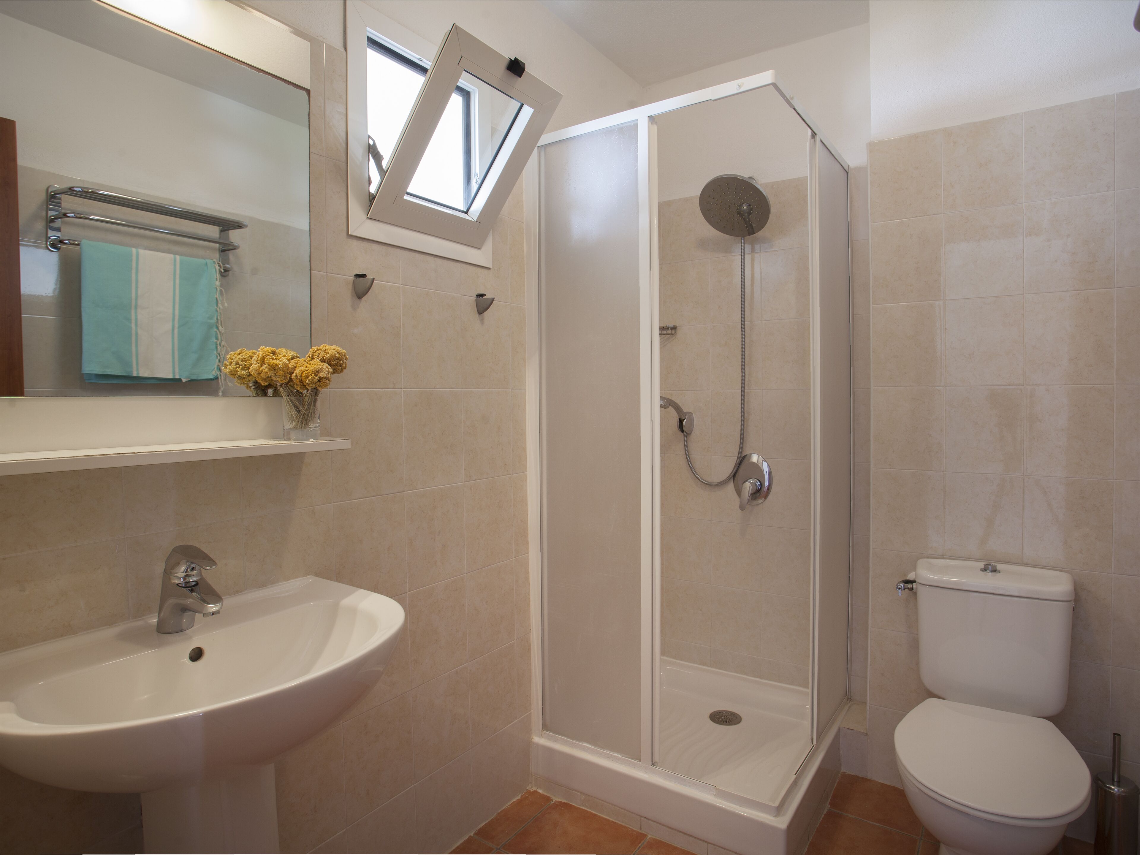 A bathroom with a shower, sink, toilet, and a window above the mirror.