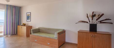 A room with a green sofa, wooden cabinets, a potted plant, and a view through a window with curtains.