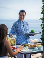 Una persona sirviendo comida y bebidas en una mesa al aire libre con vista al mar.