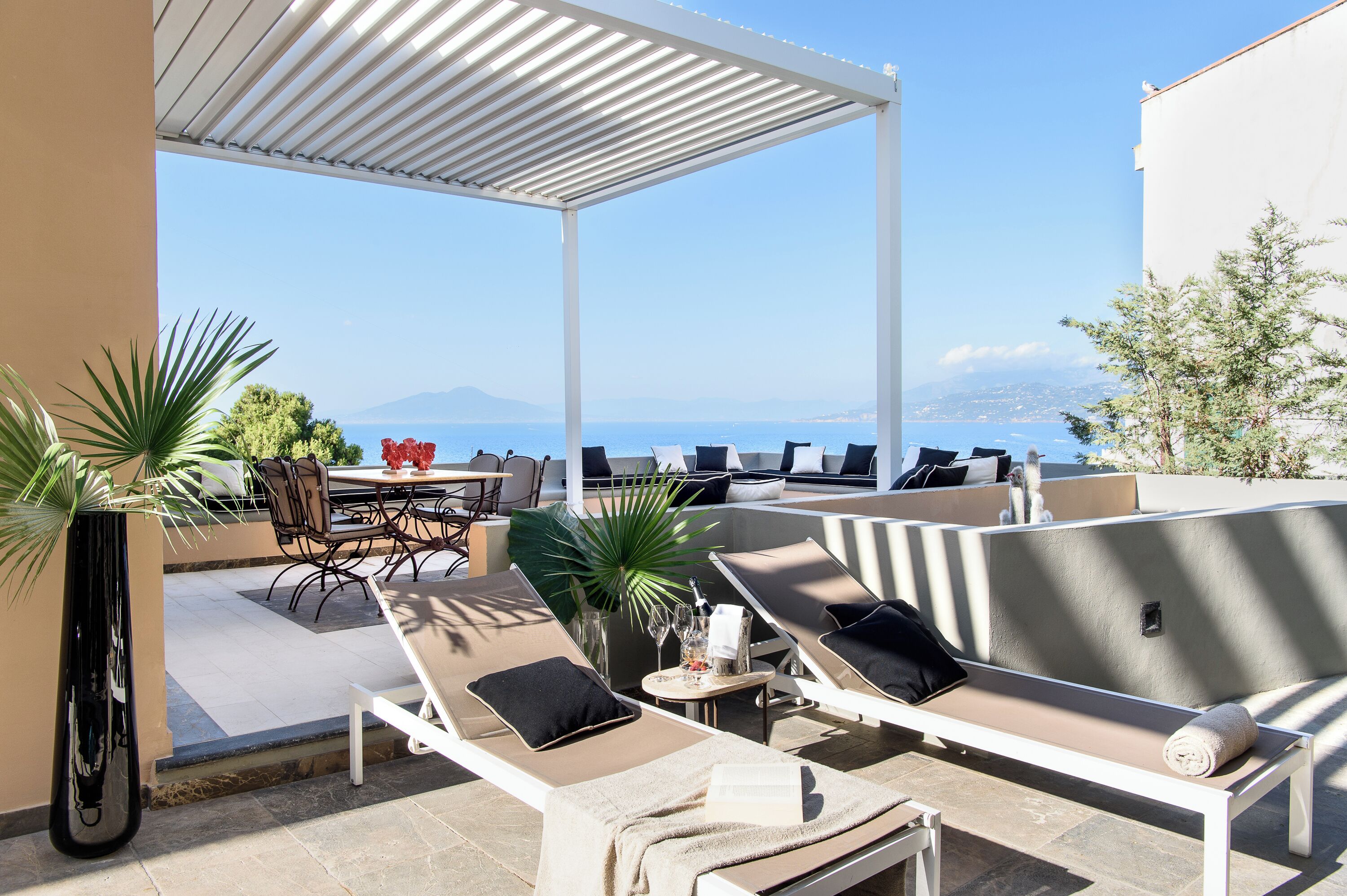 A rooftop terrace with lounge chairs, a dining table, and a view of the sea.