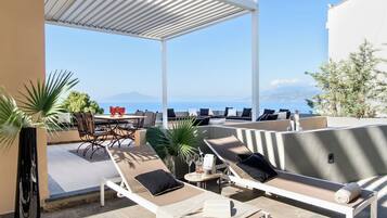 A rooftop terrace with lounge chairs, a dining table, and a view of the sea.