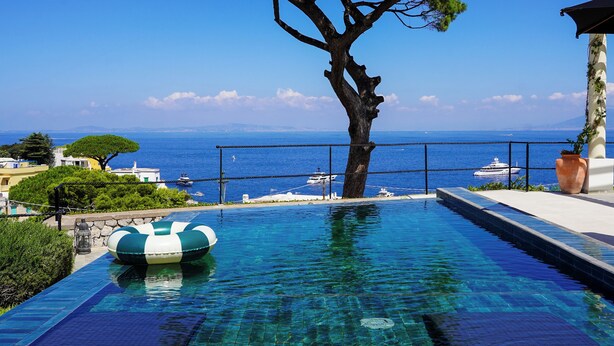 Une piscine d’un bleu éclatant, avec un arbre au centre, une vue sur la mer et un poste de surveillance pour les sauveteurs.