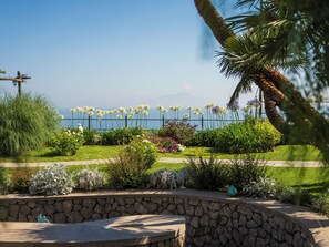 Un jardín ajardinado con muro de piedra, diversas plantas y vista al mar.