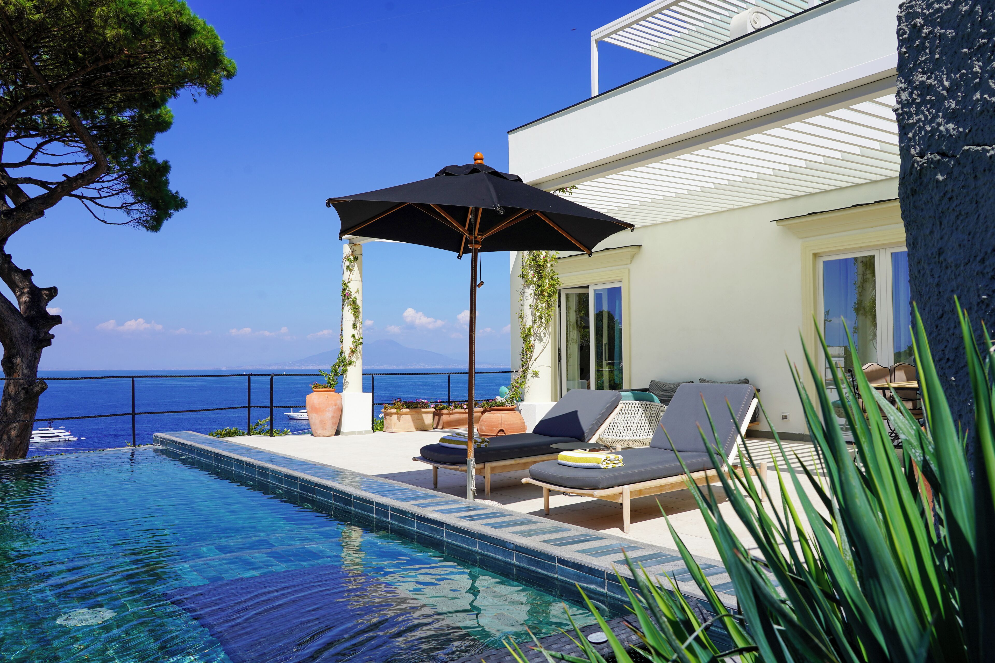 Zona de piscina con sillones, una sombrilla y vista al mar.
