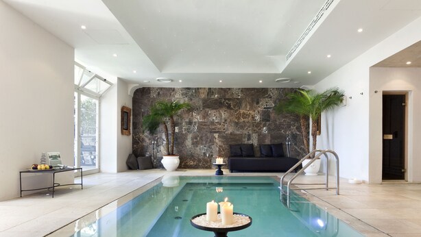 A modern indoor pool with a stone wall backdrop, a seating area with a sofa and cushions, and a small table with candles. - Villa Marina Capri - Preferred Hotels & Resorts (Capri)