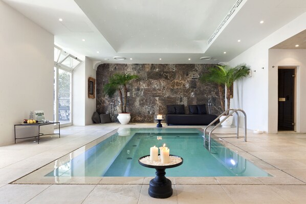 A modern indoor pool with a stone wall backdrop, a seating area with a sofa and cushions, and a small table with candles. - Villa Marina Capri - Preferred Hotels & Resorts (Capri)