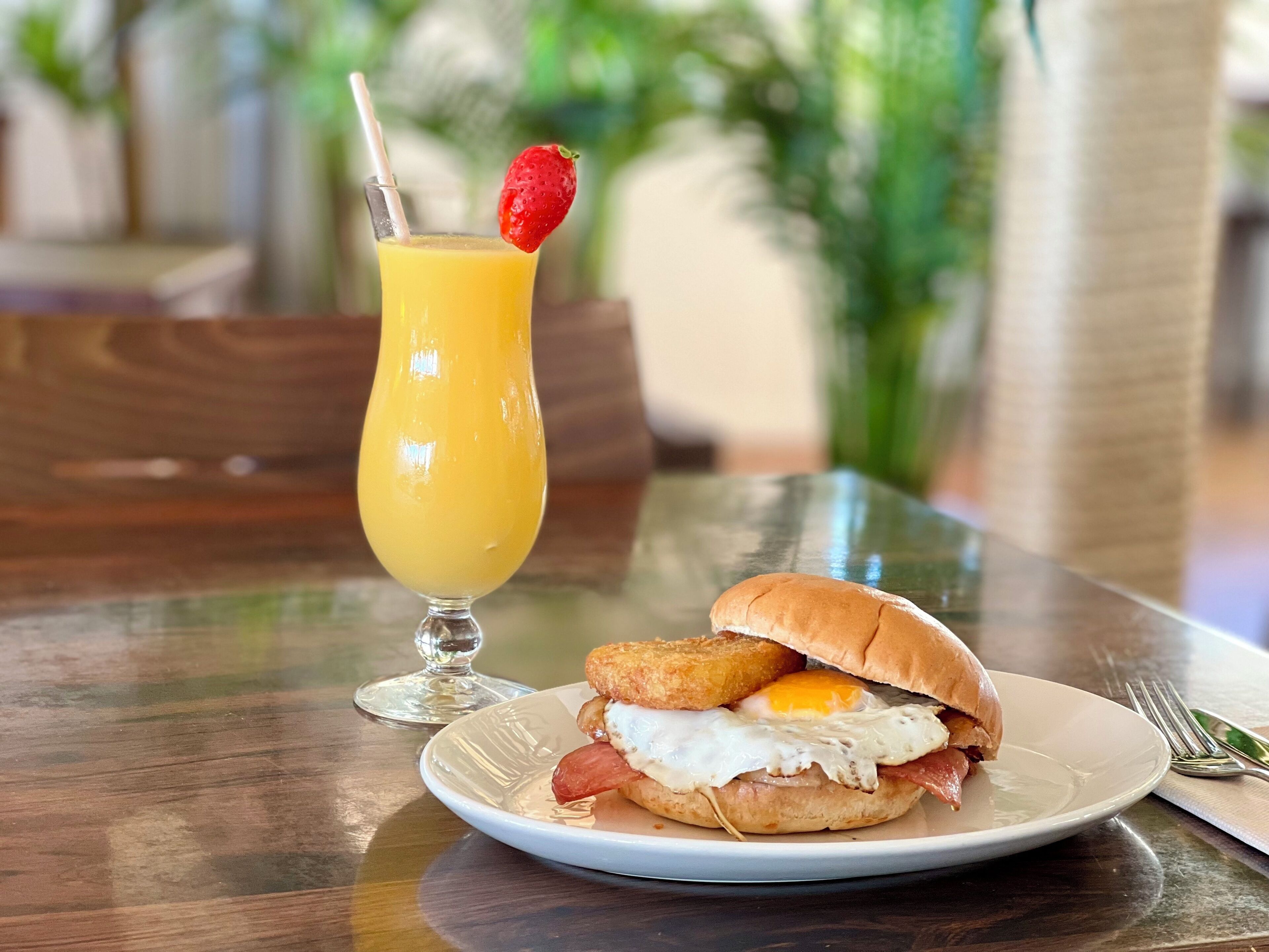 A breakfast plate with a sandwich, a glass of orange juice, and a straw.