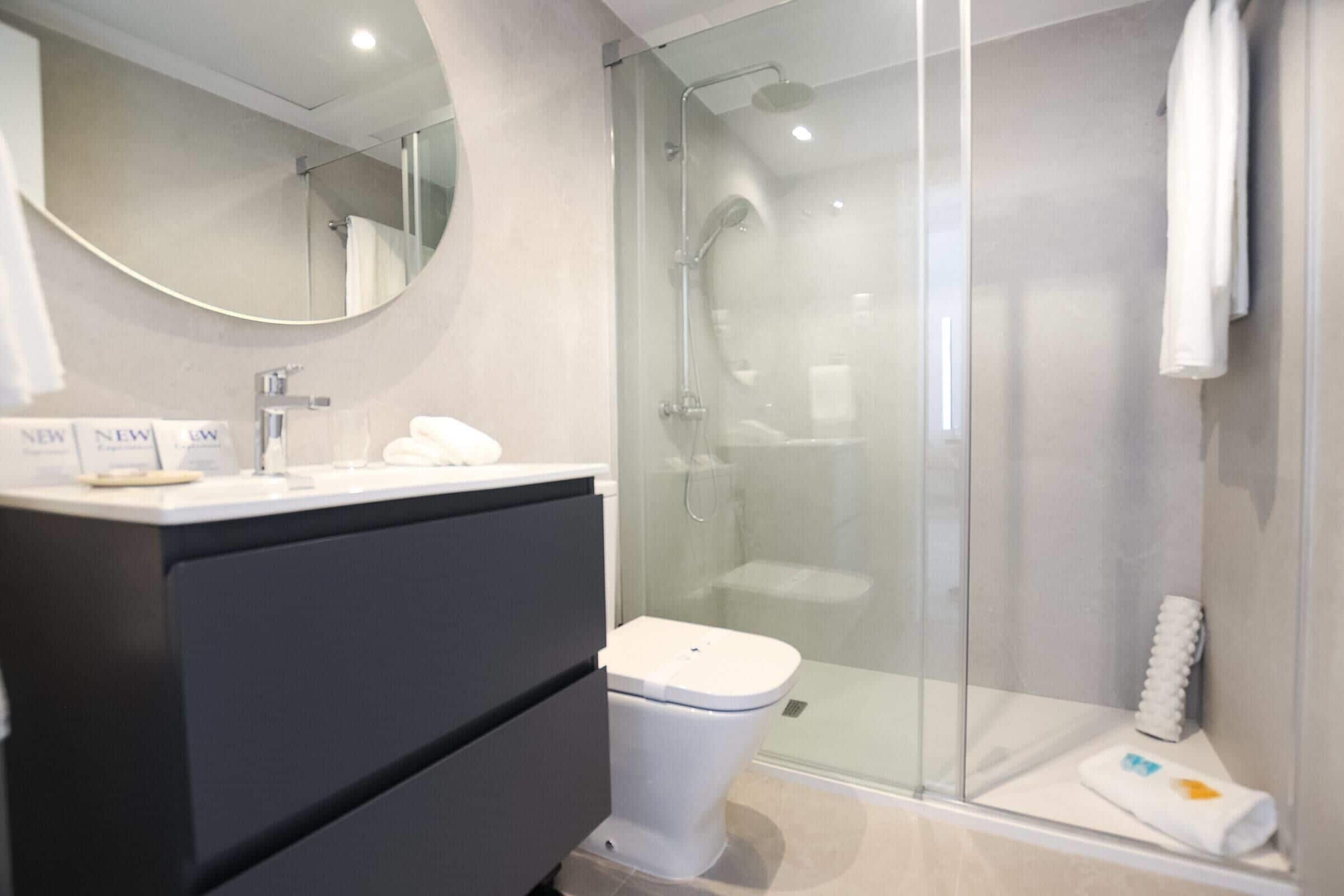 Une salle de bain moderne avec une douche à parois de verre, des toilettes blanches et un meuble-lavabo avec un miroir.