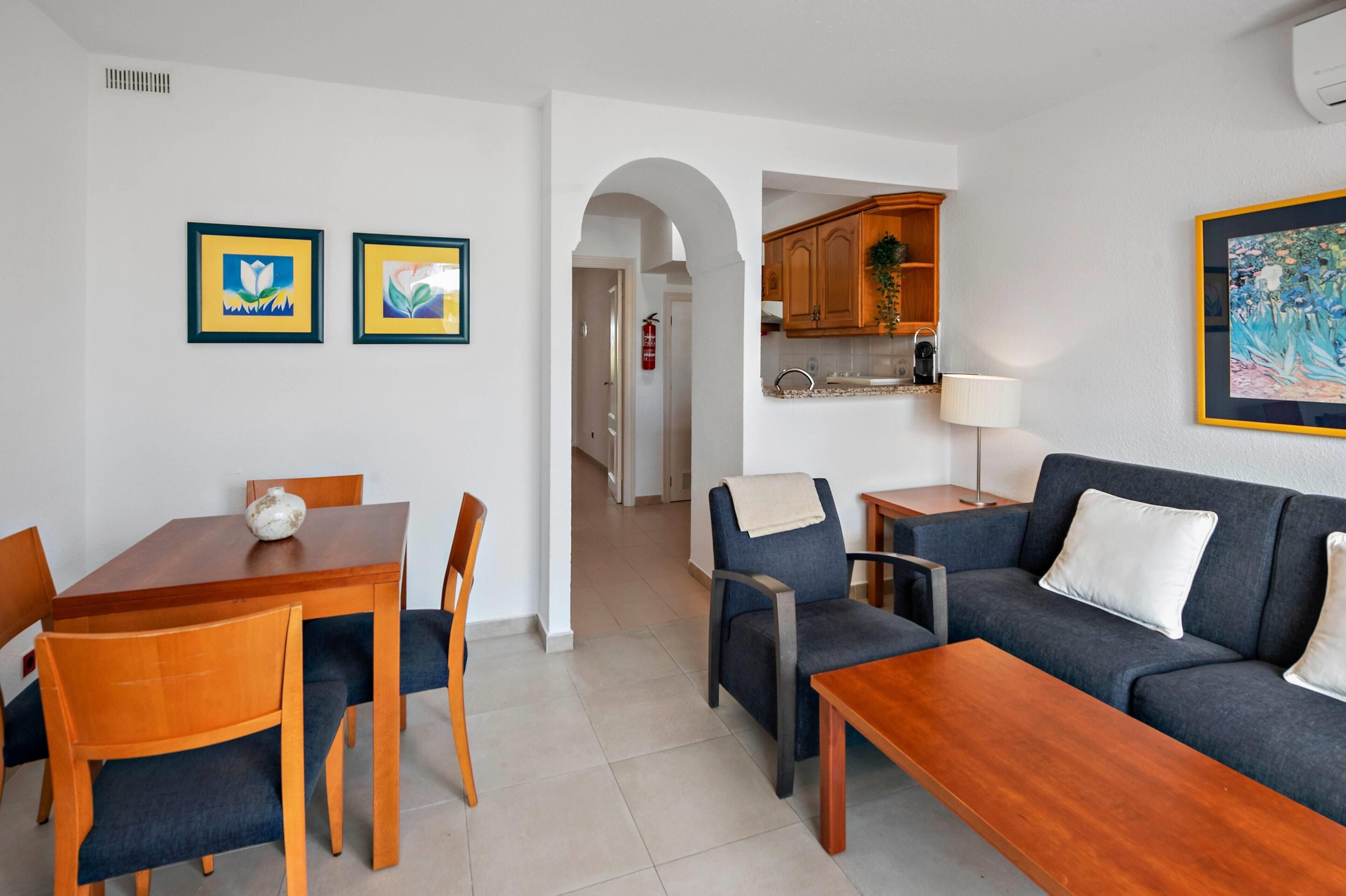 A modern living room with a sofa, coffee table, dining table, chairs, and artwork on the walls.