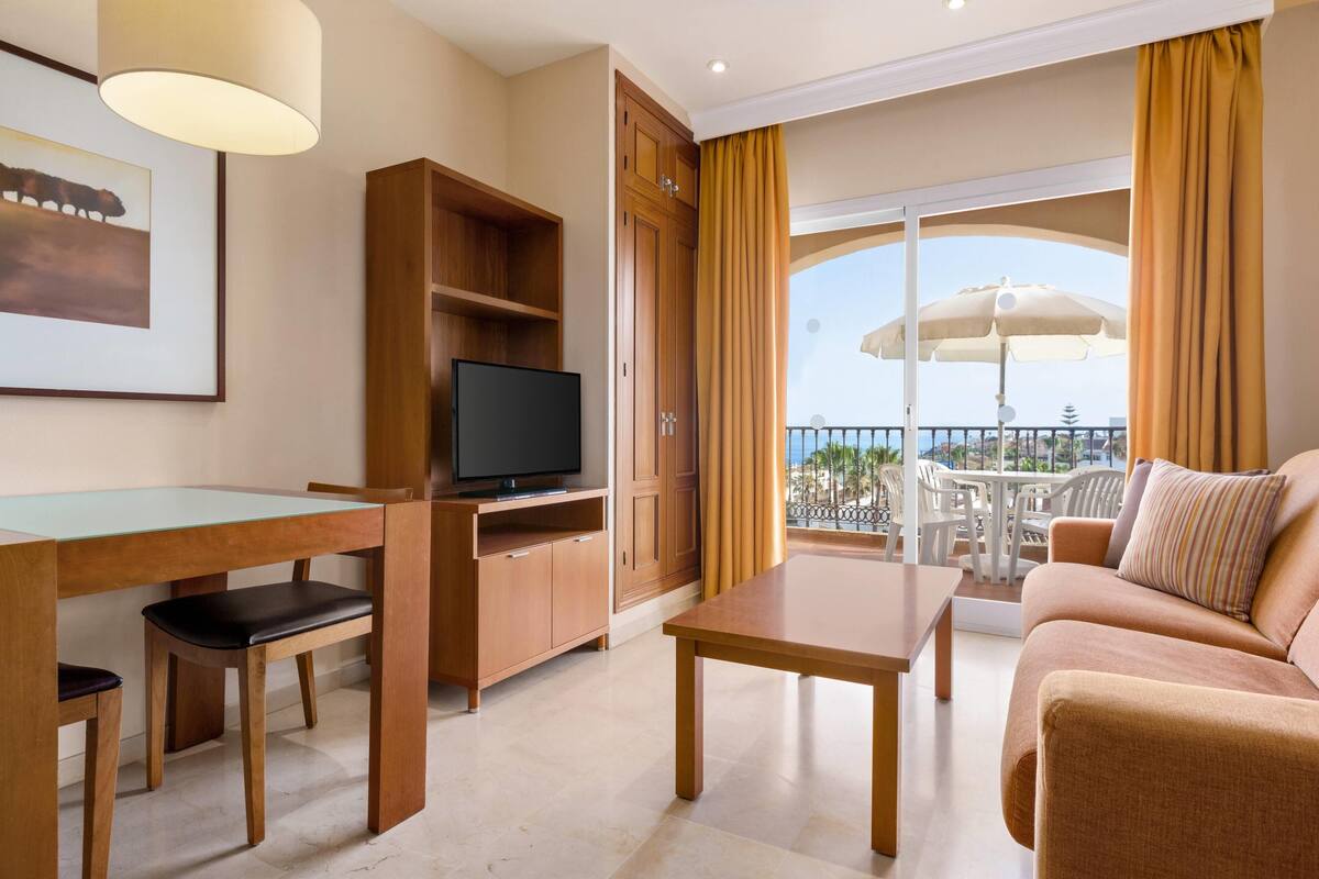 Habitació d'hotel amb balcó, televisió, taula de dinar i sofà.