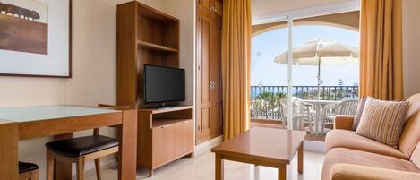 Quarto de hotel com varanda, televisão, mesa de jantar e sofá.