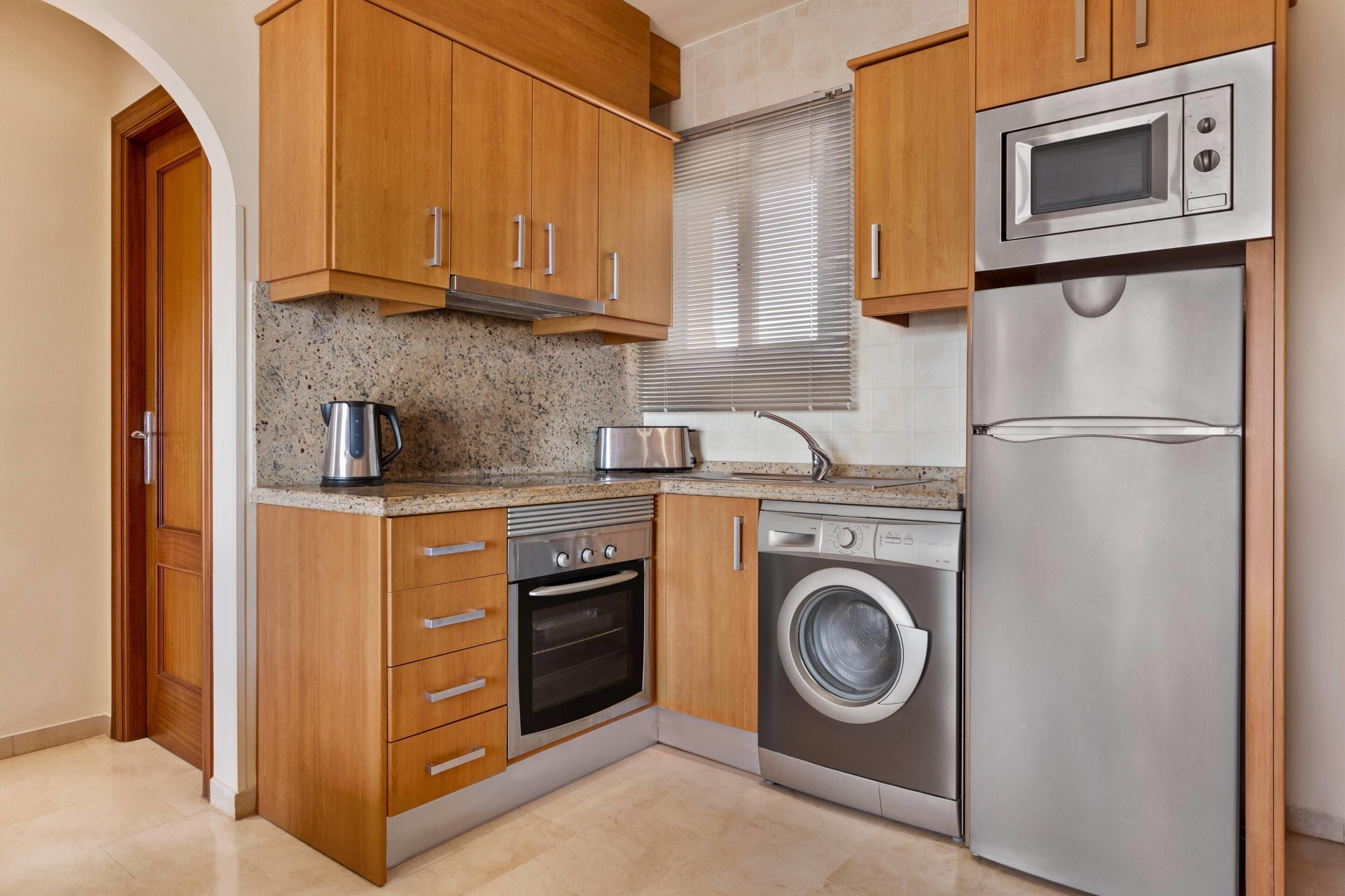 A kitchen with wooden cabinets, a stainless steel oven, a washing machine, and a microwave.