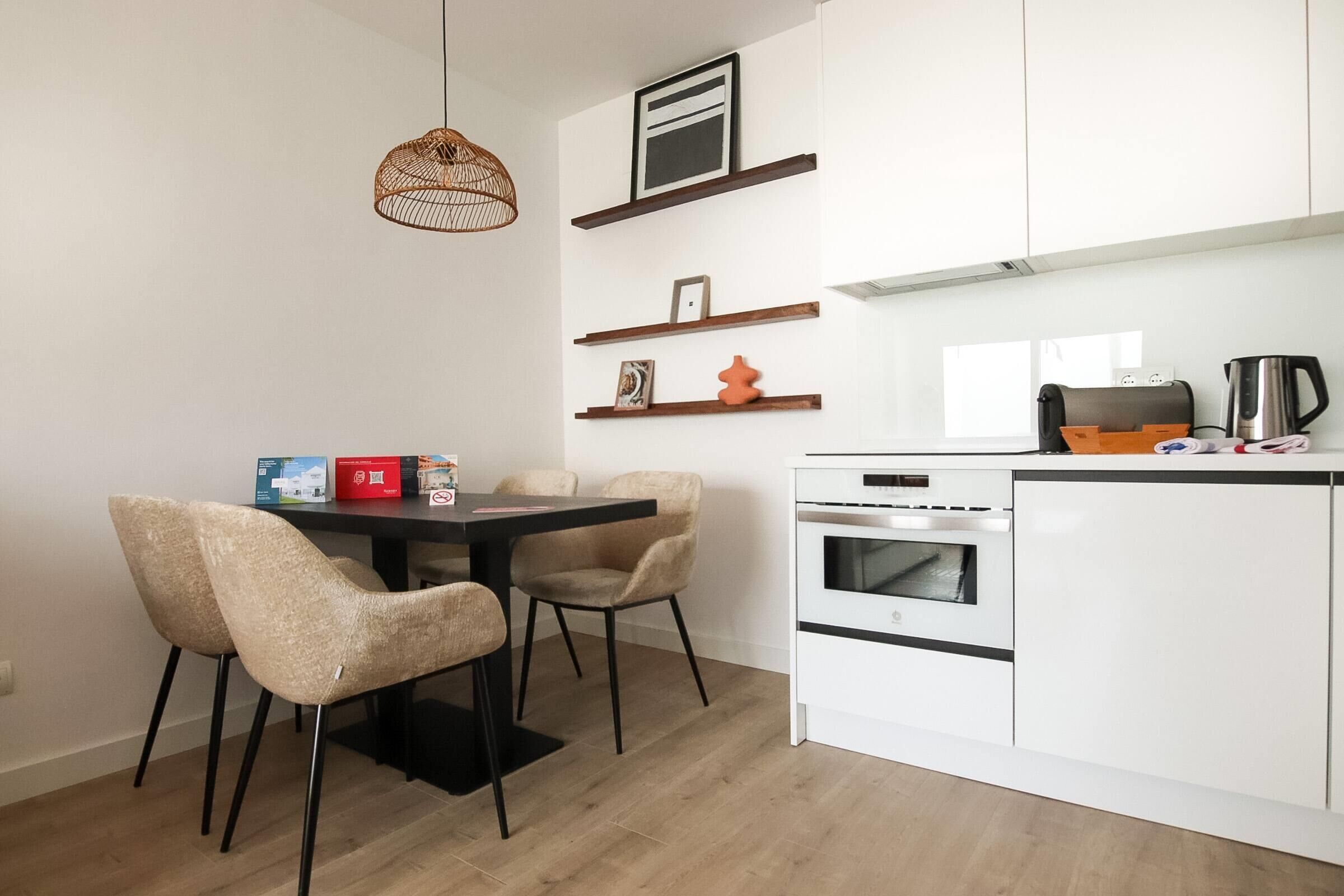 A modern kitchen with white cabinets, a dining table with chairs, and a hanging light fixture.