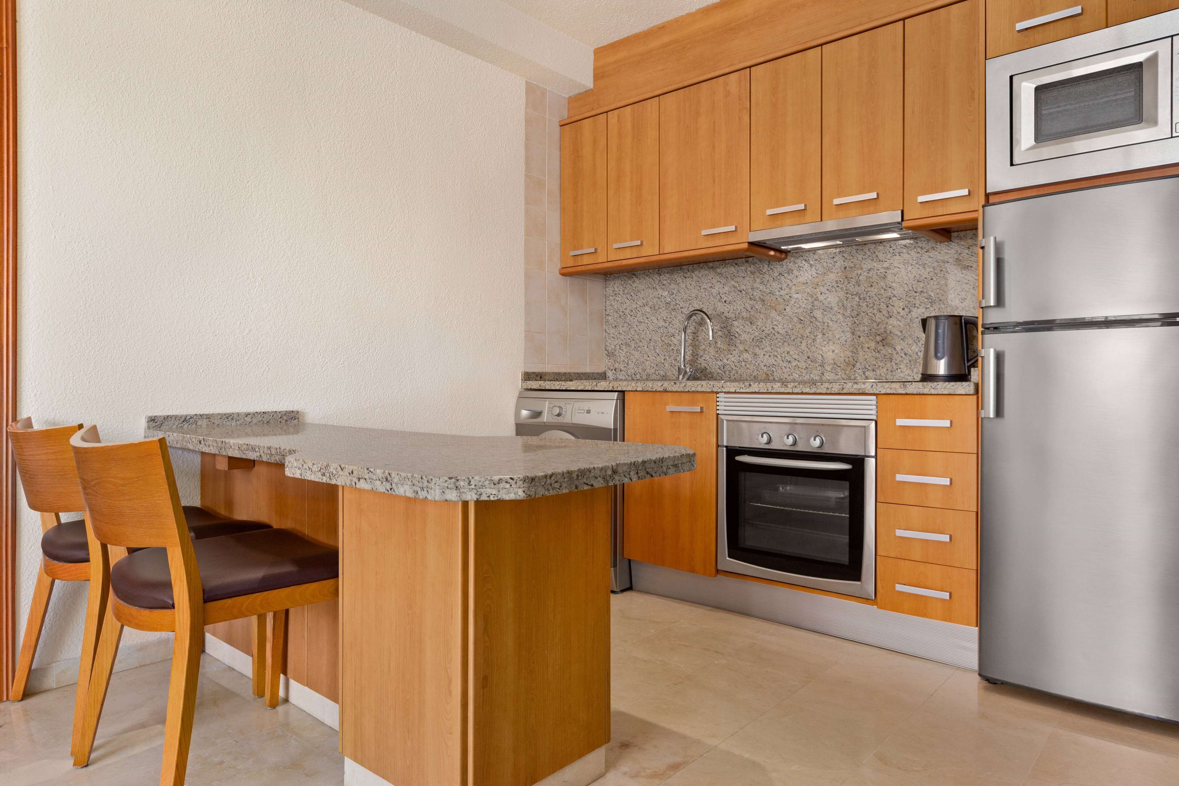 Una cocina moderna con armarios de madera, encimera de granito, horno empotrado y refrigerador de acero inoxidable.