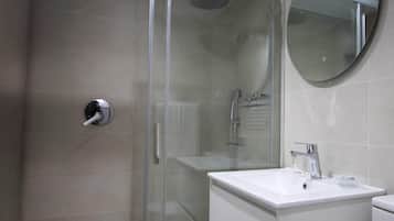 A modern bathroom with a glass-enclosed shower, a white sink with a chrome faucet, and a round mirror on the wall.