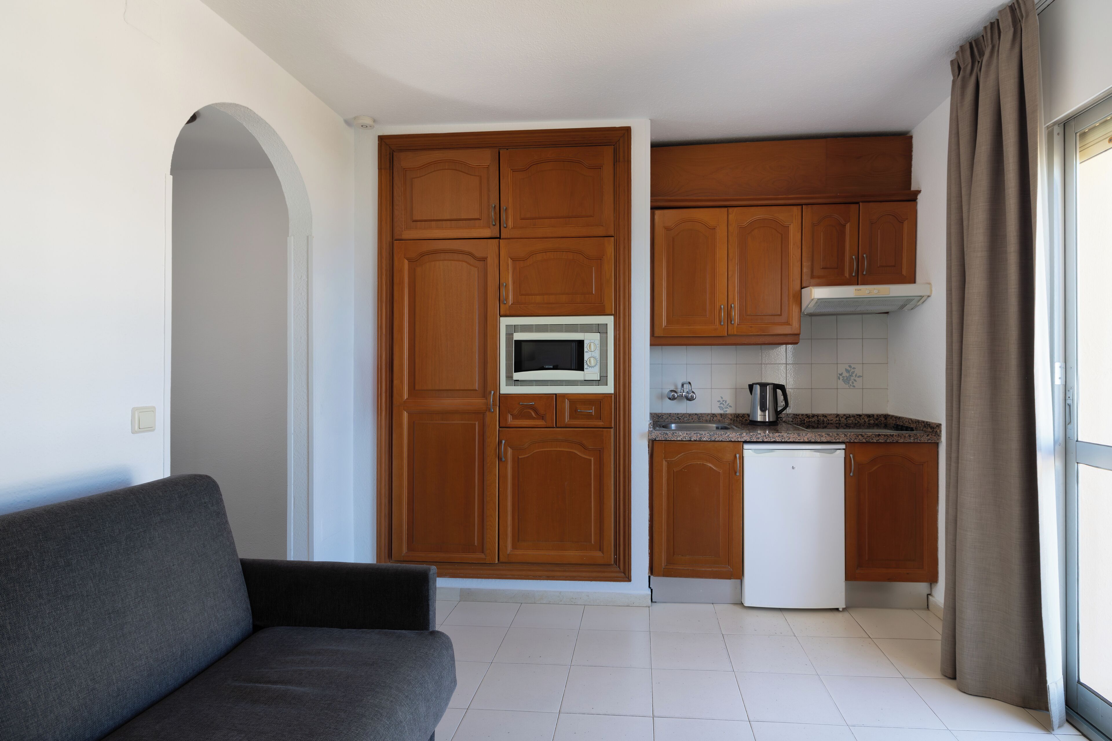 Una cocina compacta con armarios de madera, microondas integrado y lavavajillas blanco.