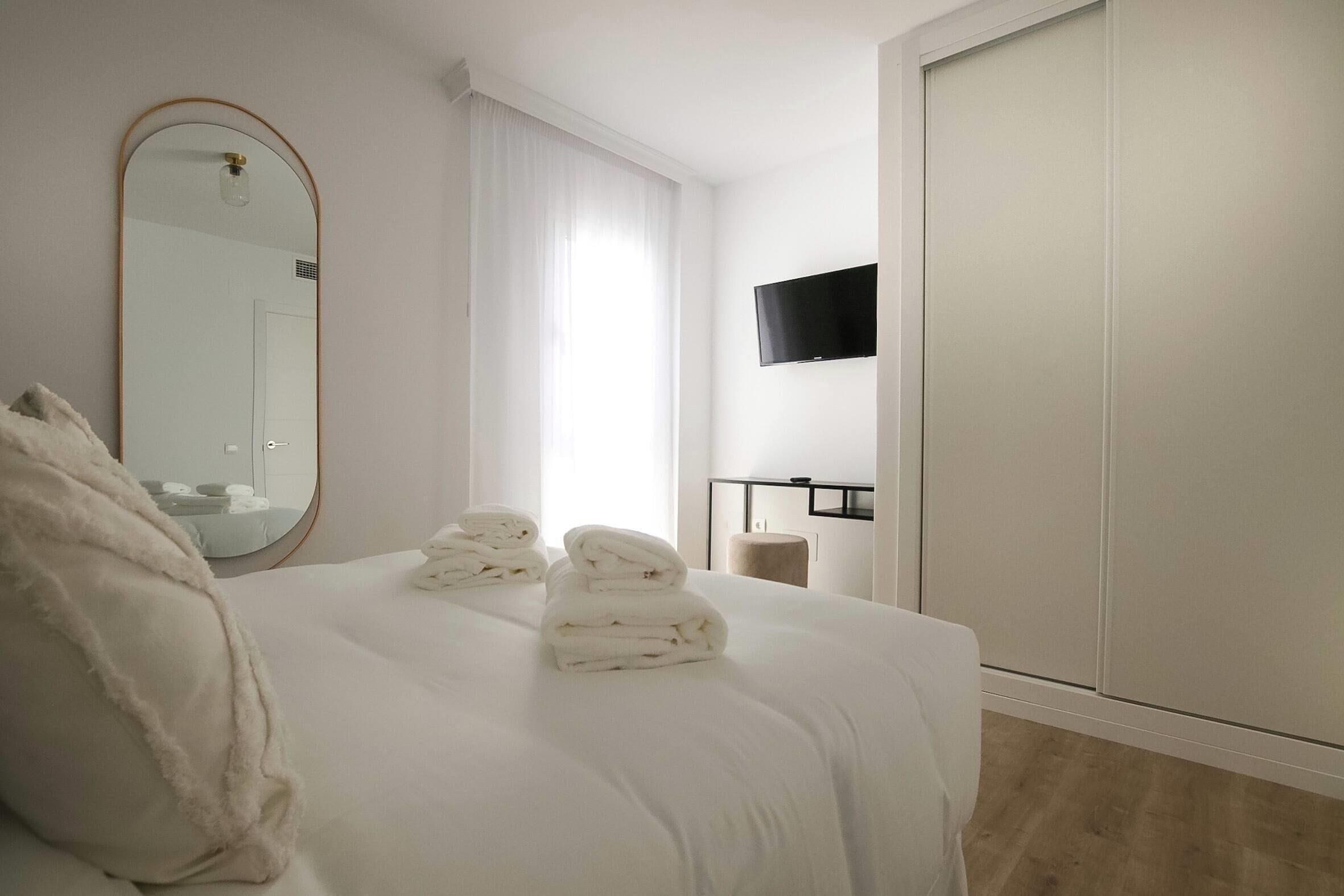 A hotel room with a bed, a large mirror, a TV mounted on the wall, and a wardrobe.