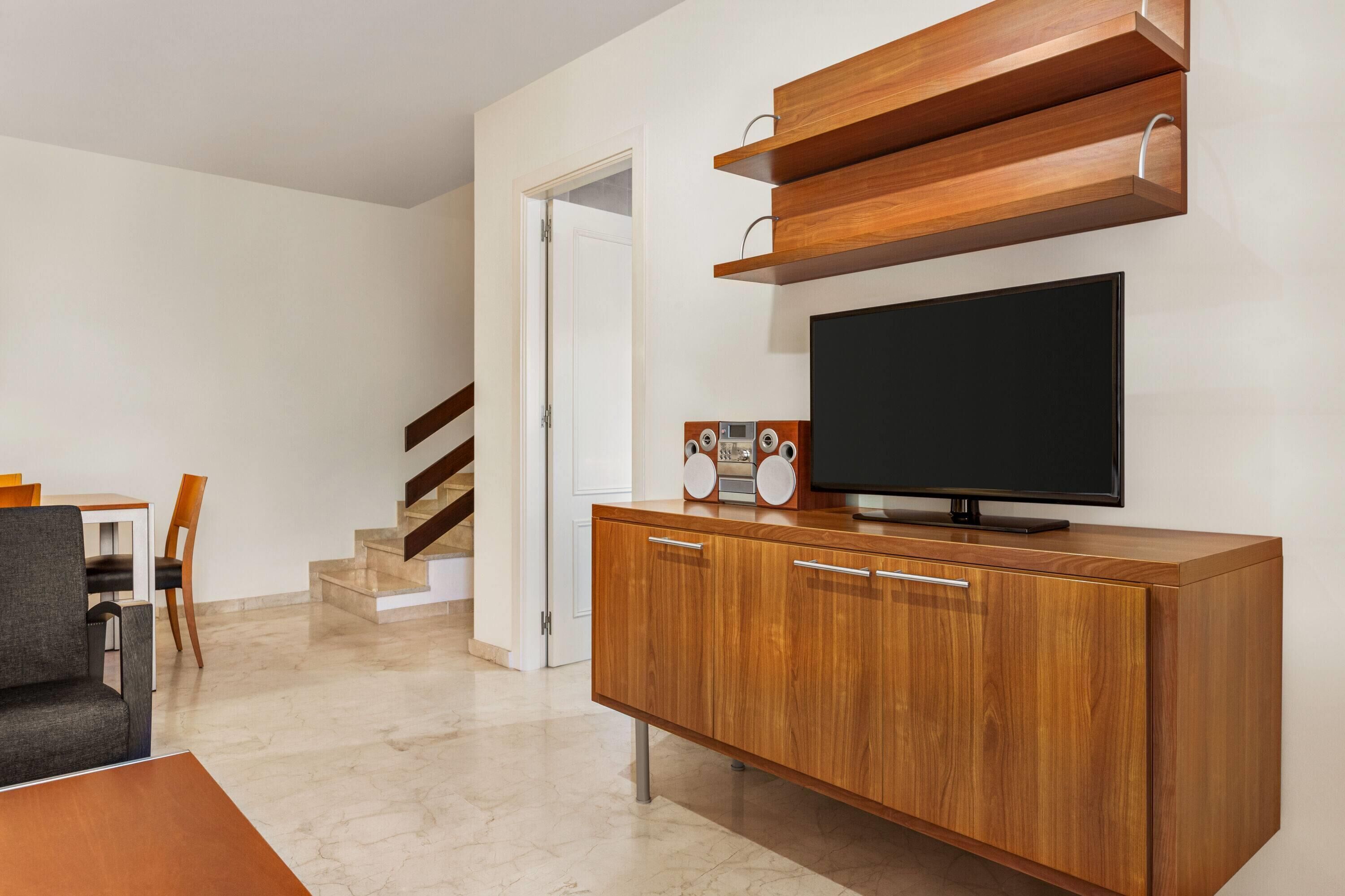 A modern living room with a wooden cabinet, a flat-screen TV, and a staircase.