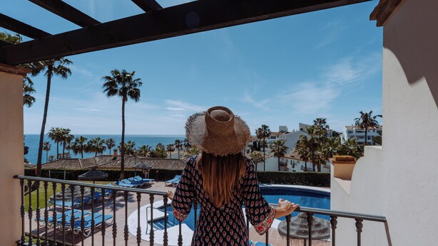Un balcón con vista a un área de piscina, palmeras y edificios al fondo.