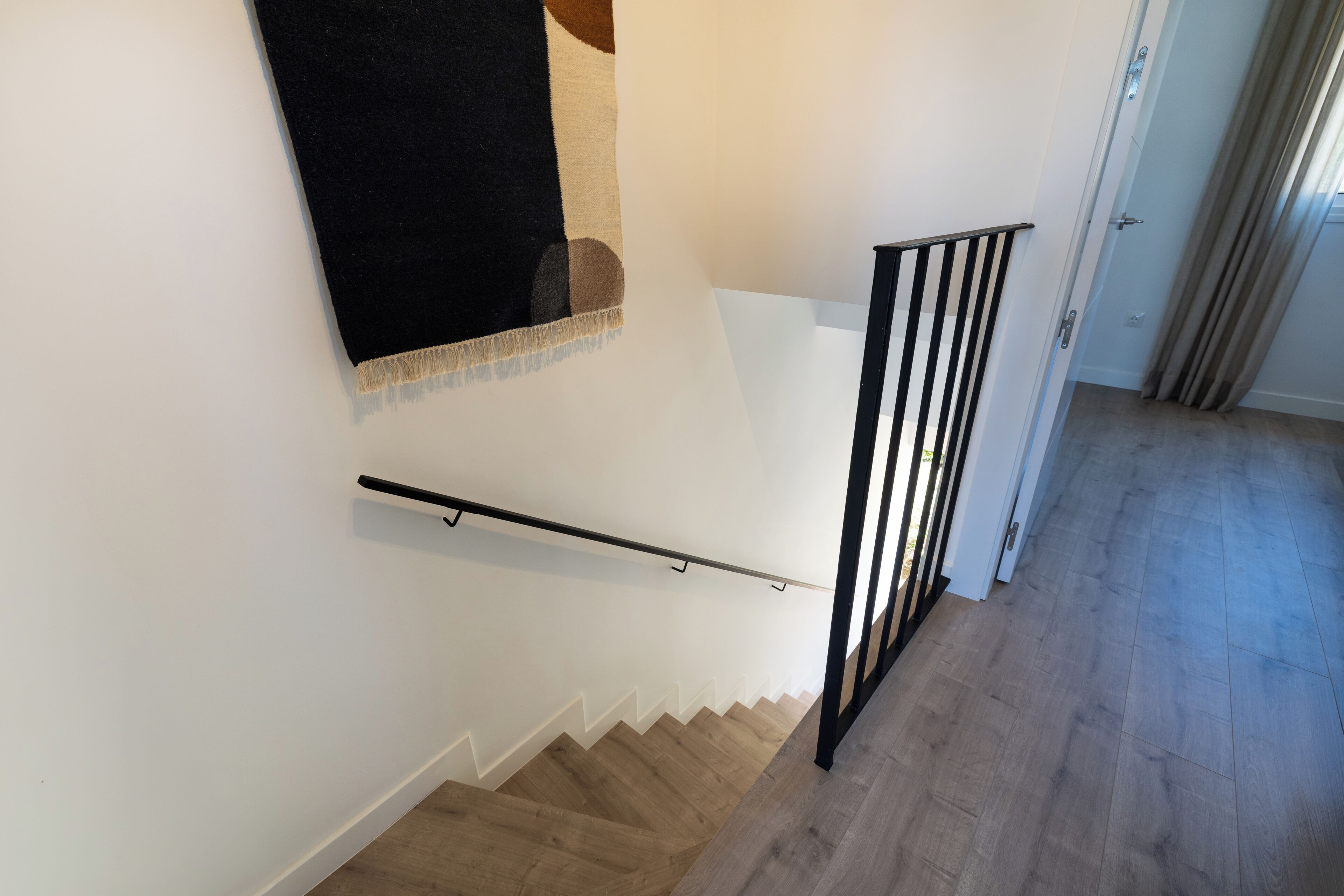 A staircase with a black handrail, wooden steps, and a white wall.