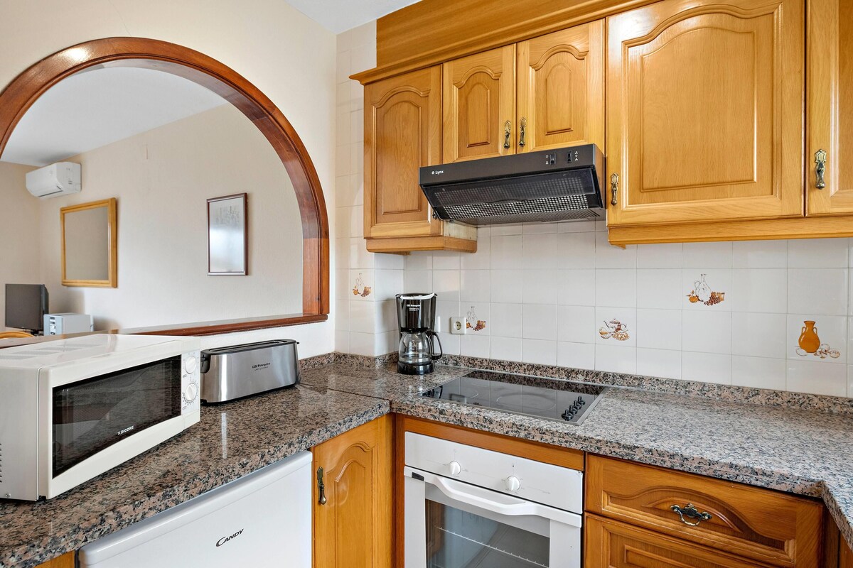 A kitchen with wooden cabinets, a microwave, a toaster, a coffee maker, and a stove.