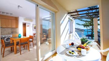 Een balkon met een eettafel gedekt voor twee personen, een wasmachine en een keuken met kastjes en een spoelbak.