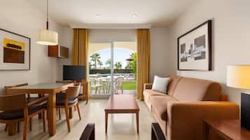 Une chambre d’hôtel comprenant un coin repas, un canapé, une télévision et un balcon avec vue sur les palmiers.